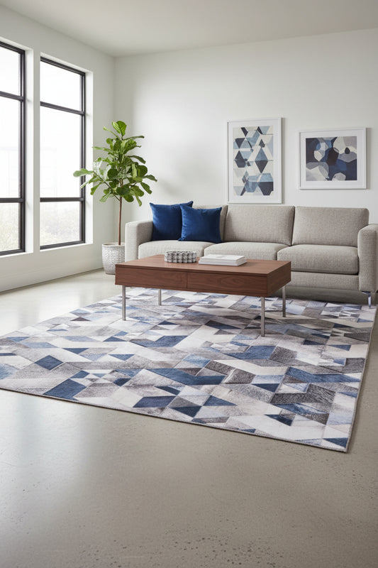 A geometric patterned rug featuring an isometric cube design in shades of blue, gray, beige, and white, with a textured cowhide-like finish.