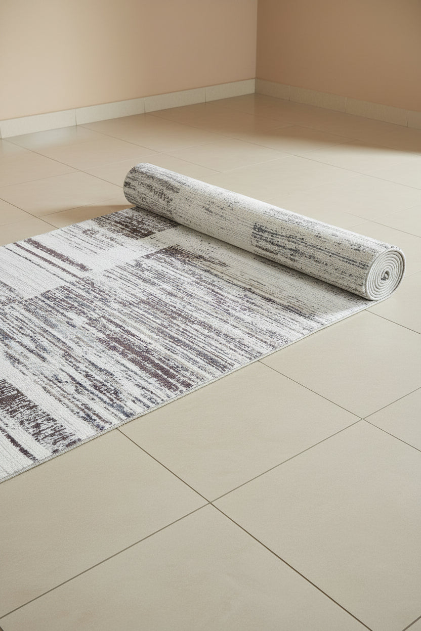 An abstract area rug featuring a distressed geometric pattern with blocks of white, gray, and muted brown.