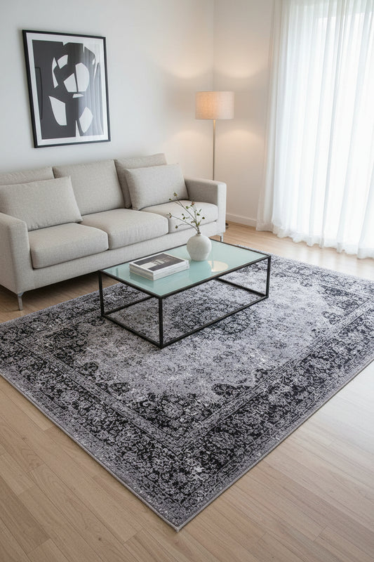 A square area rug with a distressed, vintage-style traditional pattern in shades of gray, black, and white.