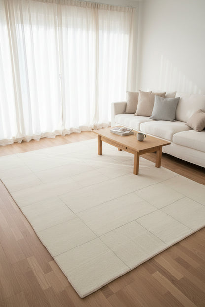 A square area rug with a modern geometric pattern of light gray and off-white rectangular blocks, creating a subtle brick or stone-mosaic effect.