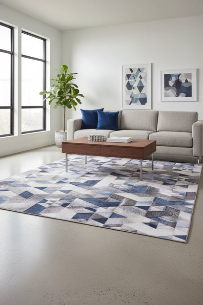 A geometric patterned rug featuring an isometric cube design in shades of blue, gray, beige, and white, with a textured cowhide-like finish.
