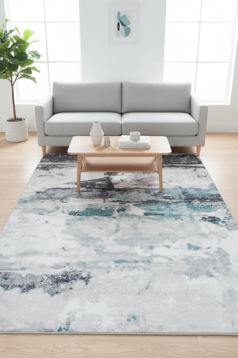 Abstract area rug featuring a textured, painterly design in white, gray, black, and teal blue.