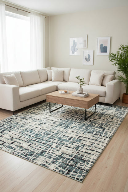 An abstract area rug featuring a distressed, cross-hatched pattern in slate blue, charcoal gray, and cream.