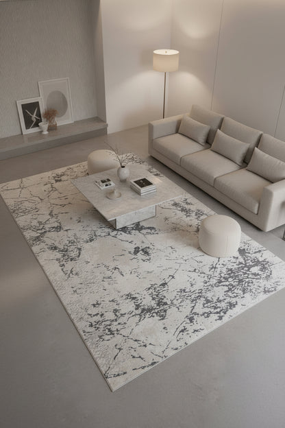 A square area rug with an abstract distressed pattern in cream, beige, and charcoal gray.
