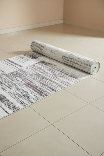 An abstract area rug featuring a distressed geometric pattern with blocks of white, gray, and muted brown.
