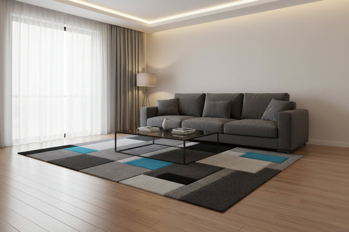 A modern geometric area rug featuring a block pattern in shades of gray, black, and white, accented with two bright teal blue squares, shown from an elevated perspective on a white background.