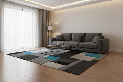 A modern geometric area rug featuring a block pattern in shades of gray, black, and white, accented with two bright teal blue squares, shown from an elevated perspective on a white background.